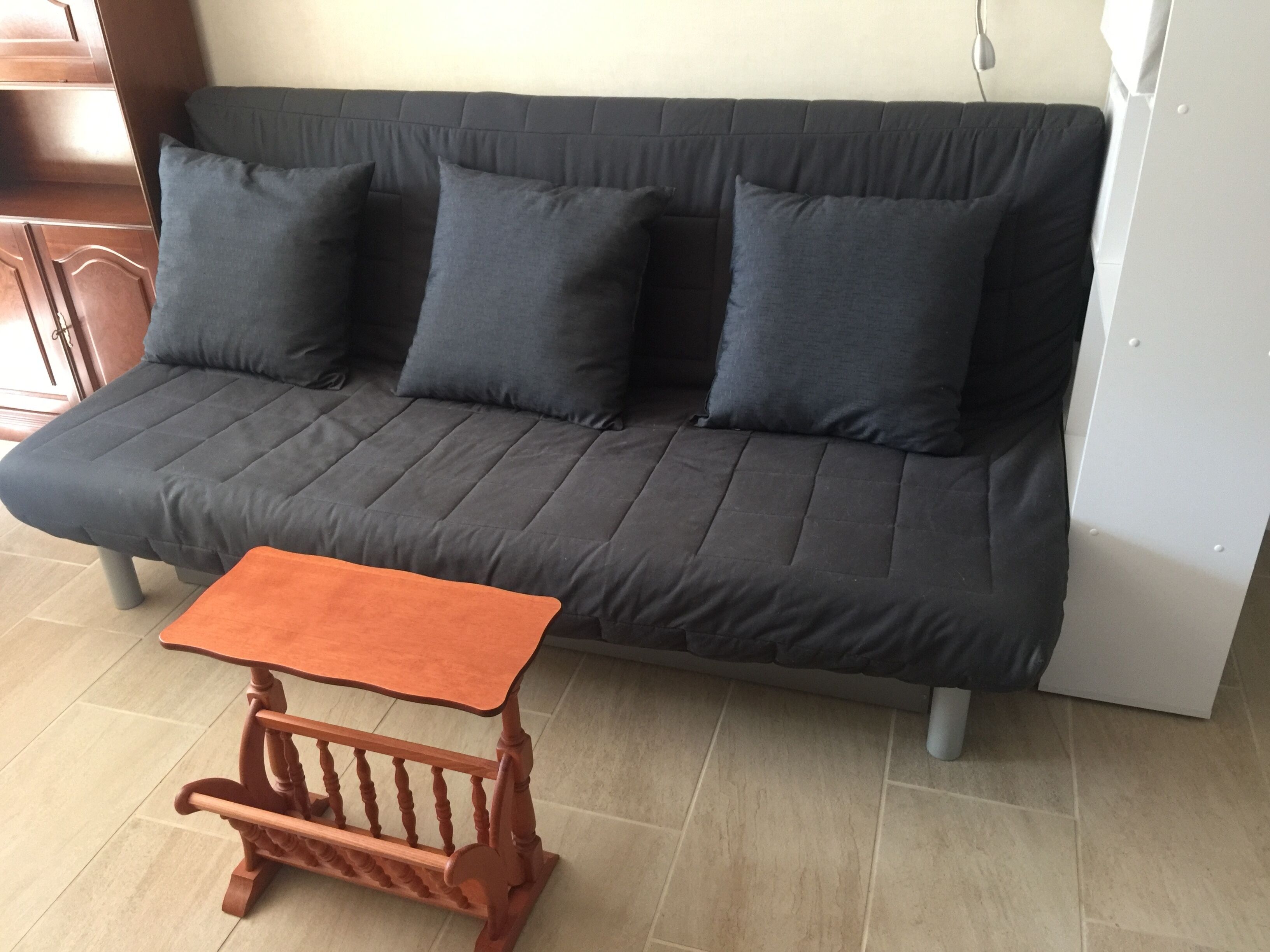 Ein dunkelgraues Sofa mit vier Kissen, ein kleiner Holztisch mit rechteckiger Tischplatte und eine weiße Kommode zur Rechten.