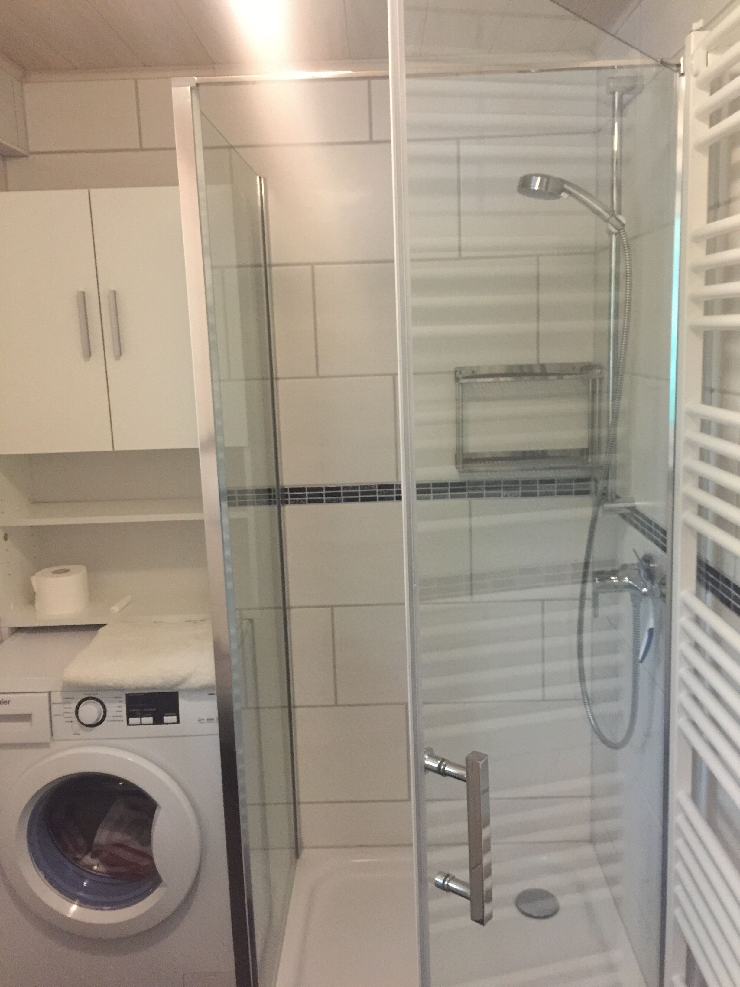 A bathroom with a glass-enclosed shower, a washing machine, and a toilet.
