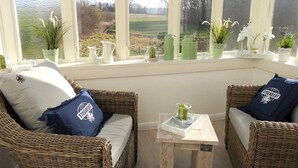 A cozy seating area with wicker chairs and cushions, a small table with a candle, and a view of a rural landscape through large windows. - "NATÜRlich Wassermühle" Vacation Home in Kappeln (Kappeln)