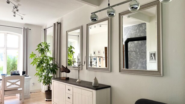 A modern living room with a white cabinet, a black sofa, and three large mirrors on the wall. - "NATÜRlich Wassermühle" Vacation Home in Kappeln (Kappeln)