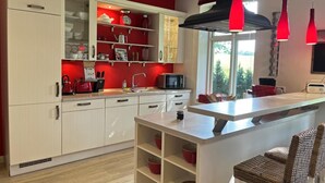 A modern kitchen with white cabinets, red accents, and a central island with seating. - "NATÜRlich Wassermühle" Vacation Home in Kappeln (Kappeln)