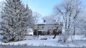A house with a snow-covered yard and a frozen lake in the foreground. - "NATÜRlich Wassermühle" Vacation Home in Kappeln (Kappeln)