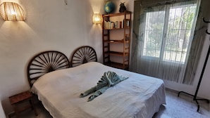 Een keurig opgemaakt slaapkamer met een bed, nachtkastjes, een boekenplank en een raam met gordijnen.