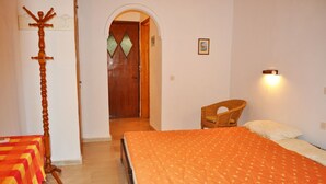 A room with a bed, a chair, a coat rack, and a door leading to another room.