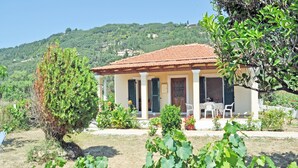 A house with a red-tiled roof, a porch with a table and chairs, and a garden with grapevines.