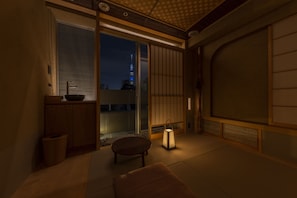 Une pièce de style japonais traditionnel, avec un sol recouvert de tatamis, une porte coulissante, une petite table, une lanterne et une vue sur un paysage urbain avec une tour.