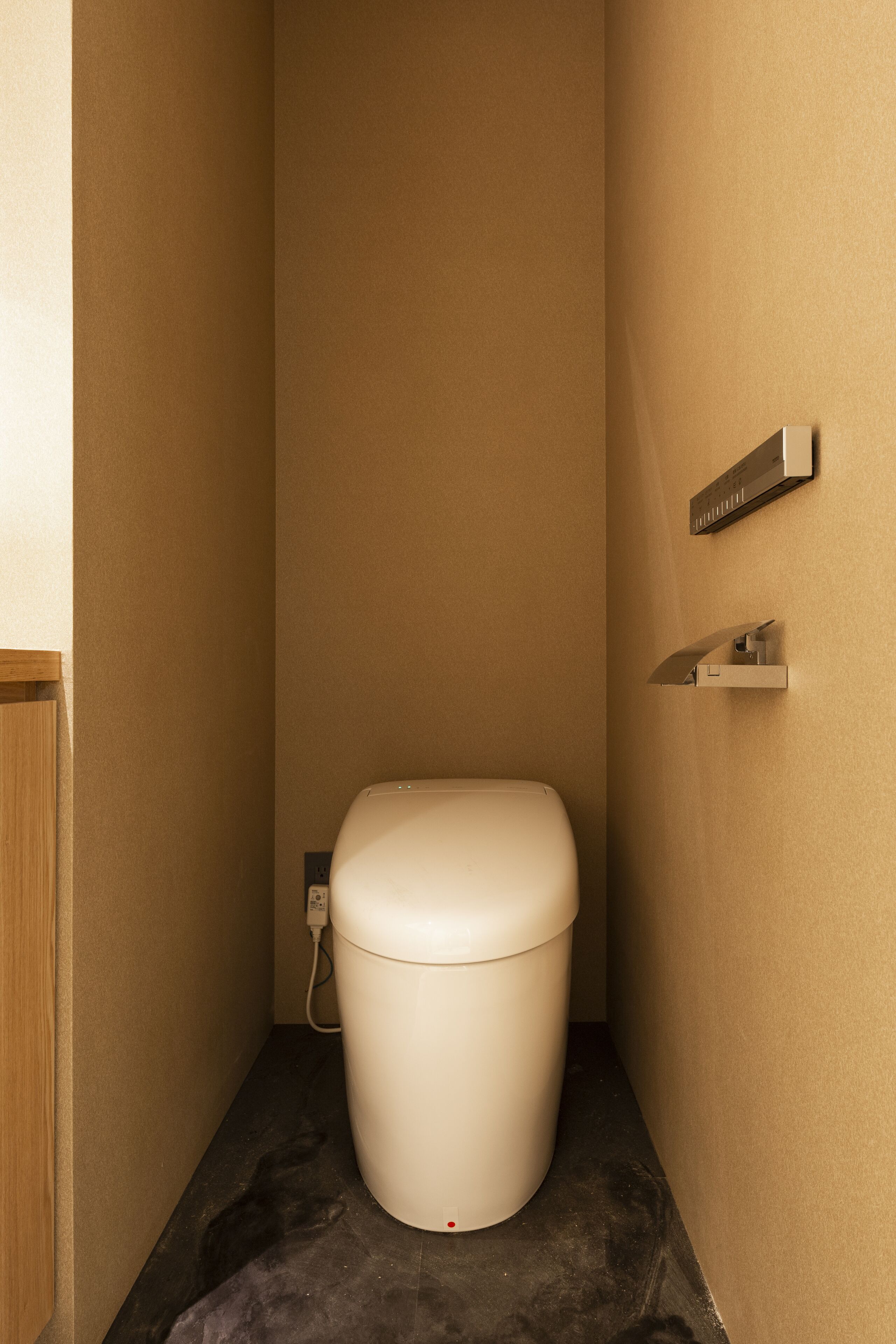 A small, narrow bathroom with a toilet, a wall-mounted shelf, and a power outlet.