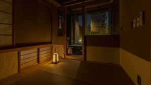 Una habitación japonesa tradicional con suelo de tatami, un puertas correderas que dan a un balcón y un farol que ilumina el espacio.