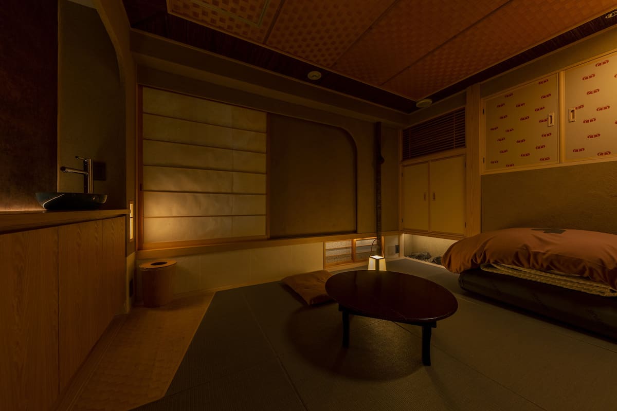 A traditional Japanese-style room with tatami flooring, a low table, a futon bed, and sliding doors.