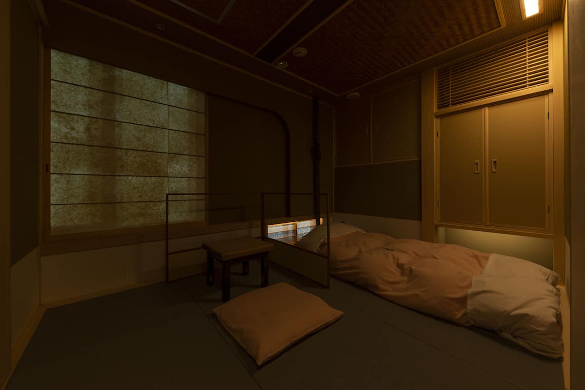 A traditional Japanese room with tatami flooring, a low bed with a futon, a small table, and a sliding door.
