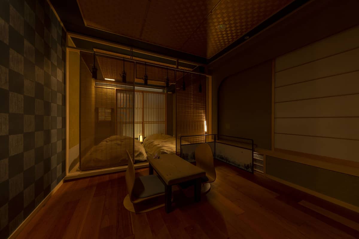 A traditional Japanese-style room with tatami flooring, a low table, a chair, and a futon bed.