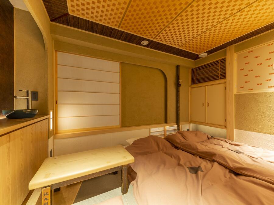 A room with a bed, a bench, a wooden cabinet, and a wall with a patterned design.