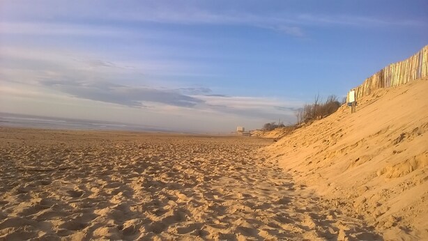 A sandy beach with a dune on the right and a clear sky.