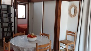 A dining area with a round table, wooden chairs, and a bowl of fruit. A staircase is visible in the background.