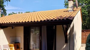 A house with a tiled roof, a covered patio with outdoor furniture, and a sliding glass door leading to an interior space.