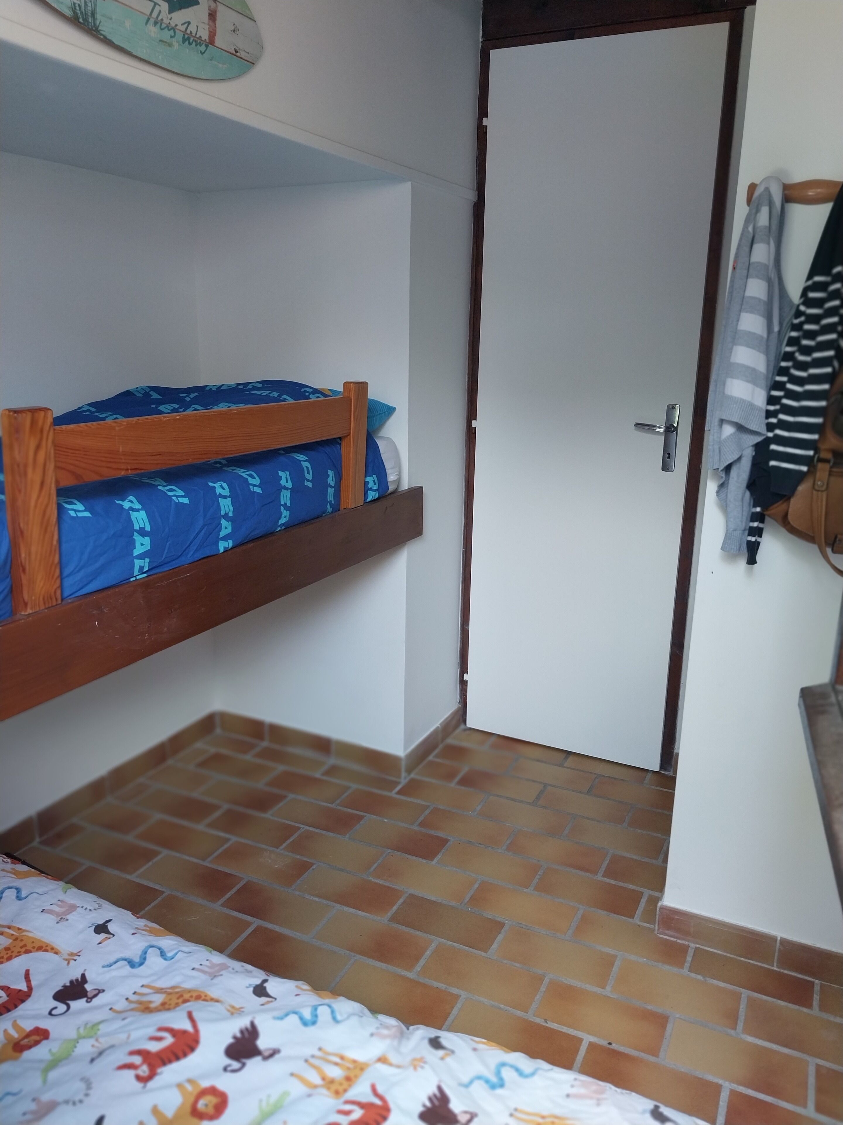 A small room with a bunk bed, a door, and a tiled floor.