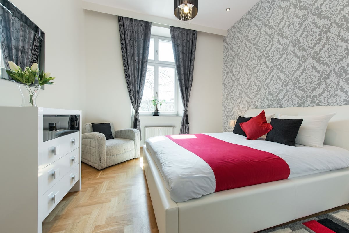 Ein modernes Schlafzimmer mit einem großen Bett, einer Kommode, einem Stuhl und einem Fenster mit Vorhängen.