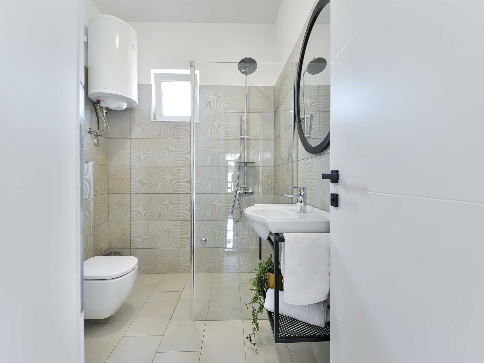 A modern bathroom with a glass shower enclosure, a white toilet, and a sink with a towel rack.
