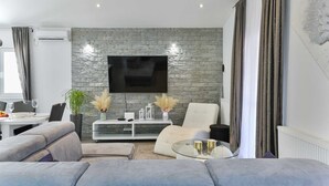 A modern living room with a stone wall, a flat-screen TV, a glass coffee table, and a sofa.