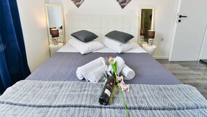 A neatly made bed with pillows, a rolled towel, a bottle of wine, and a flower. There are wall-mounted pictures with words like "LOVE" and "HOPE."