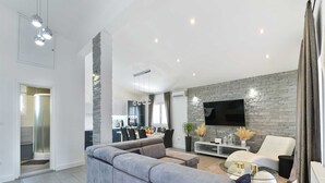 A modern living room with a grey sectional sofa, a white armchair, and a TV mounted on a stone wall.