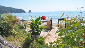 A coastal walkway with a view of the sea, a rock formation, and a gate leading to the beach.