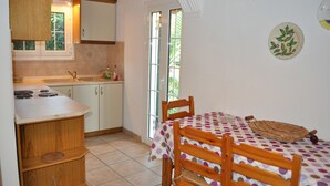 A compact kitchen with a sink, stove, and wooden cabinets. There is a dining table with a polka dot tablecloth and chairs. A wicker basket is on the table.