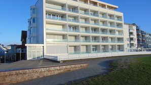 Un hotel moderno de varios pisos con fachada plana, varios balcones y un camino de ladrillo que conduce a la entrada.