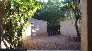 Un jardín con un camino de grava, un banco de madera y una mesa de metal.