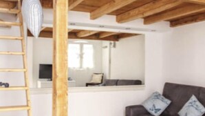 A room with a wooden ceiling, a sofa, a ladder, and a kitchen area in the background. - Studio, quiet, charming, in the heart of the old town just steps from everything (Antibes)