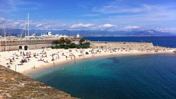A coastal beach with a stone wall, clear blue water, and boats in the background. - Studio, quiet, charming, in the heart of the old town just steps from everything (Antibes)