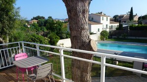 Une terrasse en bois avec une table et des chaises, d’où l’on peut admirer une piscine et une vue sur les maisons au loin.