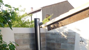 Un espace de douche carrelé en pierre, doté d’une porte en verre, entouré d’une bordure en pierre et de verdure.