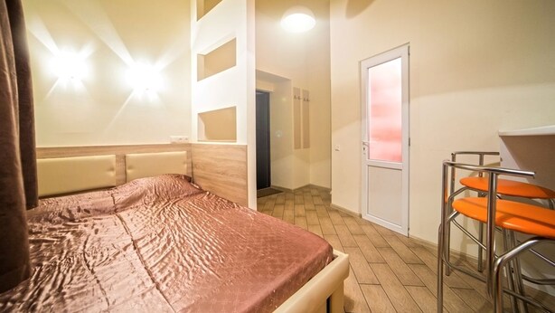 A hotel room with a bed, a desk, and a chair. There is a door leading to another room. - Smart Apartment Rappoporta 7a-1 (Lviv)