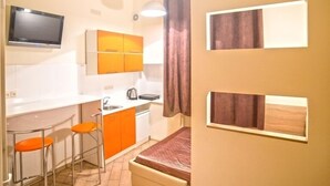 A compact kitchen with a dining area, a TV mounted above the counter, and a bed with a red blanket. - Smart Apartment Rappoporta 7a-1 (Lviv)