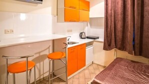A compact room with a kitchenette, a bed, and two orange bar stools. - Smart Apartment Rappoporta 7a-1 (Lviv)