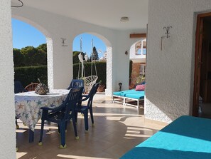 Un patio exterior con una mesa y sillas, una hamaca colgante y una cama con cubrecama azul.