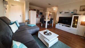 A modern living room with a dark grey sofa, a white coffee table, and a TV cabinet. - Ground floor/quiet/WLAN/terrace with garden and the sound of waves/holiday from day 1 (Börgerende)