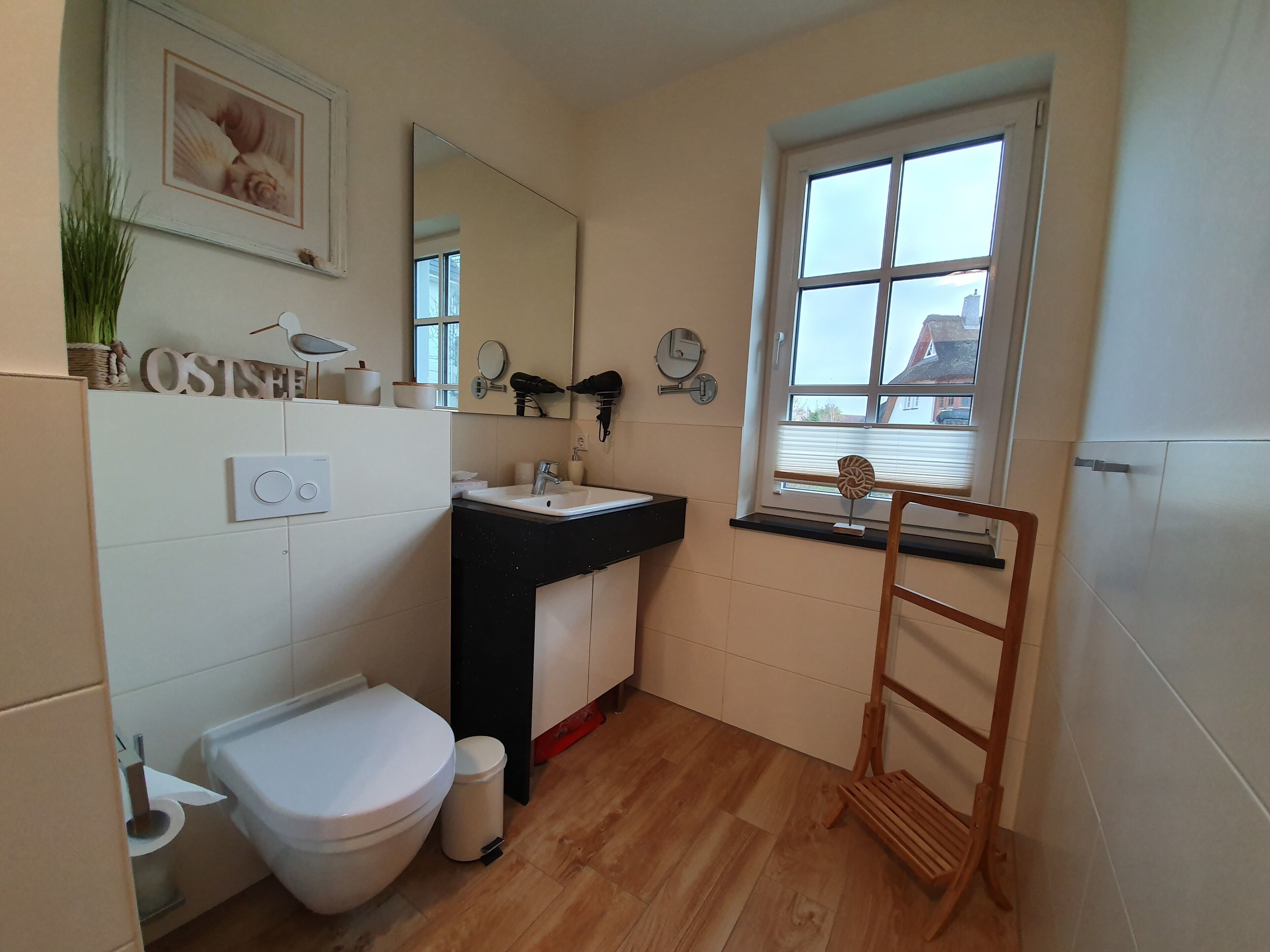 Baño con inodoro, lavamanos, espejo y ventana con vista a un edificio.