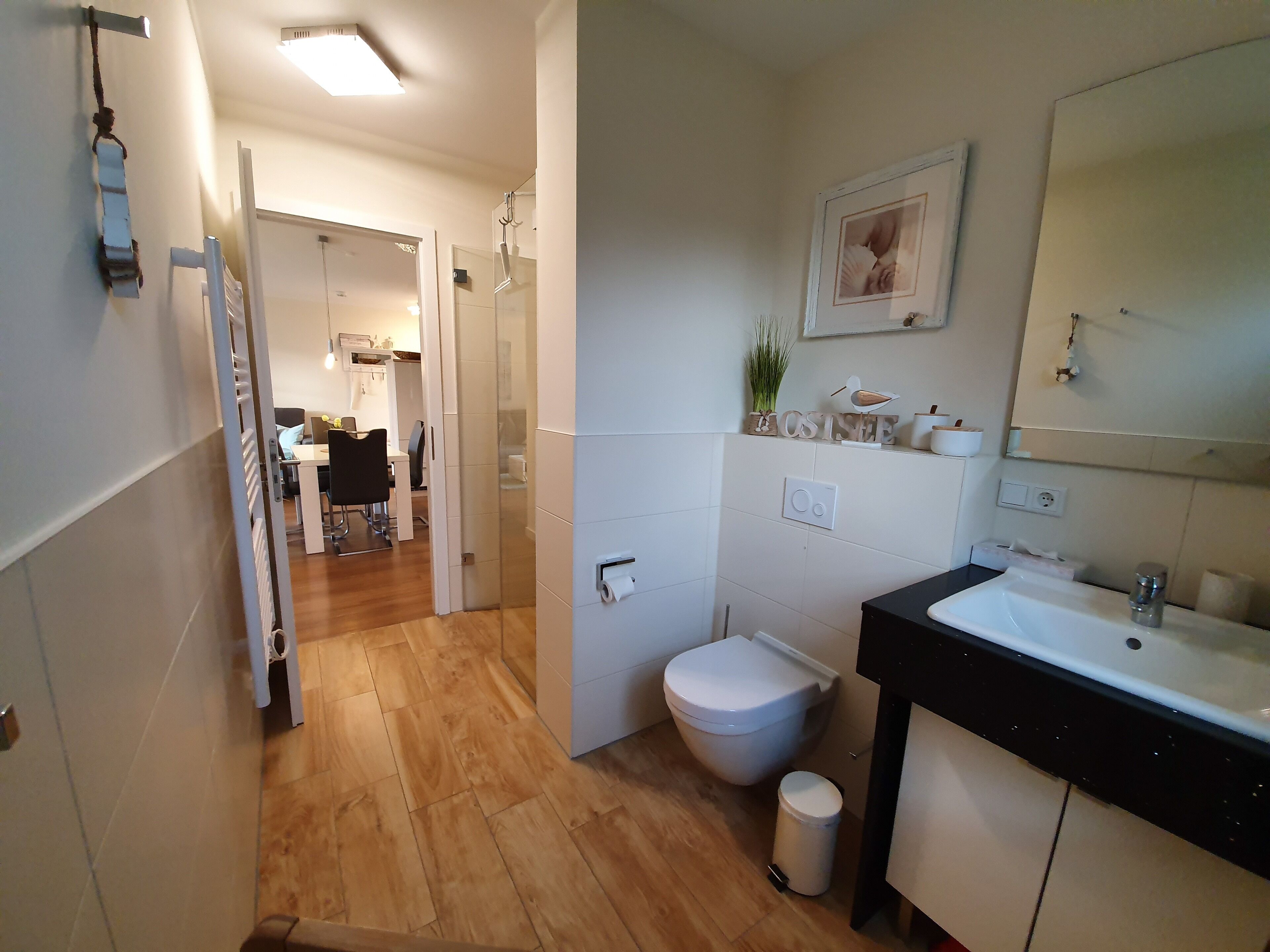 A modern bathroom with a sink, toilet, and shower area. There is a hallway leading to a dining area.