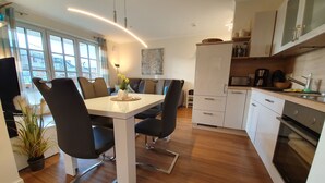 A modern kitchen with white cabinets, a dining table with chairs, and a large window providing natural light. - Ground floor/quiet/WLAN/terrace with garden and the sound of waves/holiday from day 1 (Börgerende)