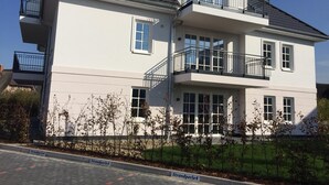A two-story residential building with a balcony on the upper floor, a garage on the ground floor, and a clear sky. - Ground floor/quiet/WLAN/terrace with garden and the sound of waves/holiday from day 1 (Börgerende)