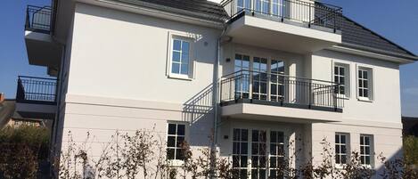 A two-story residential building with a balcony on the upper floor, a garage on the ground floor, and a clear sky.