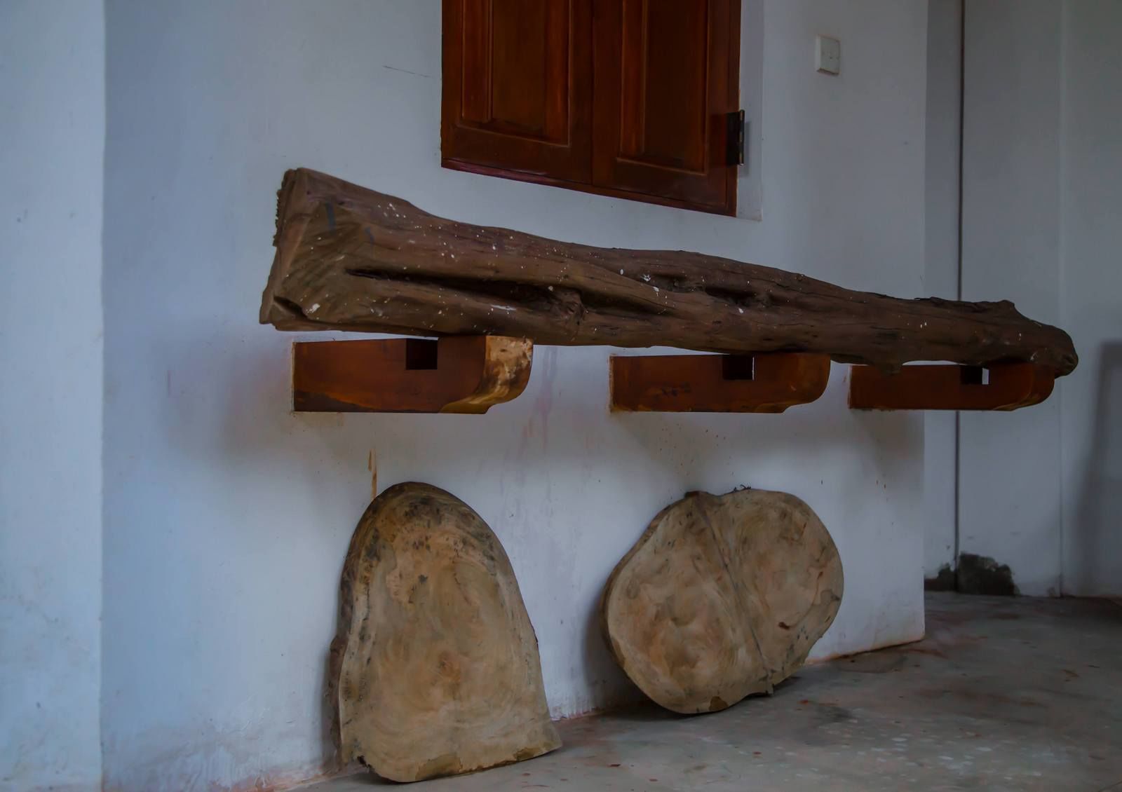 Un intérieur rustique avec une étagère en bois brut, deux grosses pierres et une porte en bois dotée d’une fenêtre.