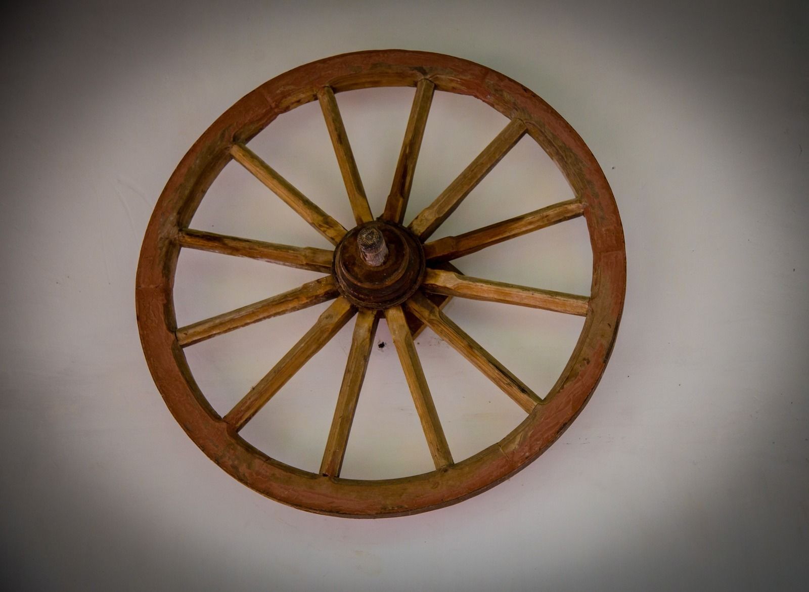 A wooden wheel with spokes and a central hub, mounted on a plain background.