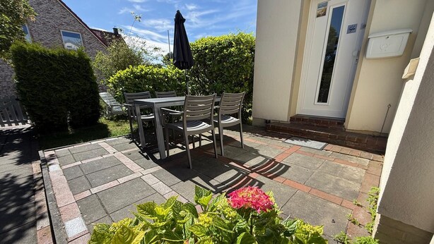 A patio with a table and chairs, a door, and a small garden with plants. - Maike - Apartment with terrace and small garden (Wangerooge)