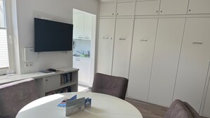 A modern room with a round white table, two brown chairs, a flat-screen TV mounted on the wall, and a white wardrobe with multiple doors. - Maike - Apartment with terrace and small garden (Wangerooge)