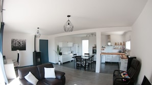 A modern living room with a brown leather sofa, a dining area with a wooden table, and a kitchen in the background. - House in Crozon between the village and the beaches. (Crozon)