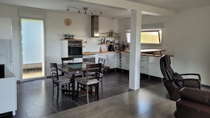 A modern kitchen with white cabinets, a dining area with a wooden table and chairs, and a large window providing natural light. - House in Crozon between the village and the beaches. (Crozon)