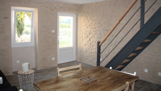 A room with a wooden table, a chair, a small round table with a candle, and a staircase with a wooden railing.